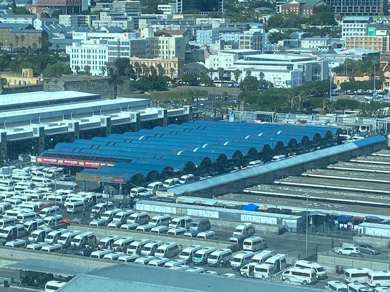 An elevated aerial view of a large transport terminal facility featuring extensive blue metal roofing and a busy parking area for commuter vehicles.