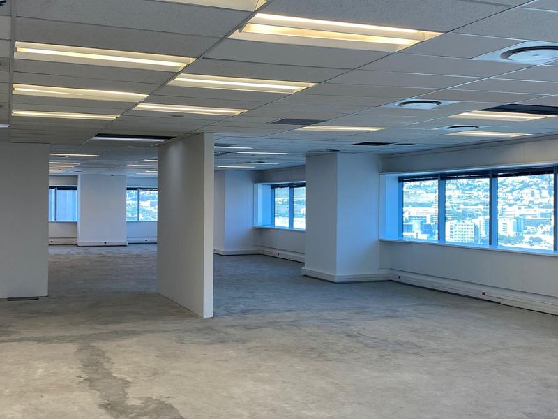 A spacious, open-plan office area featuring a suspended ceiling, recessed lighting, and large windows with expansive city views, ready for custom fit-out.