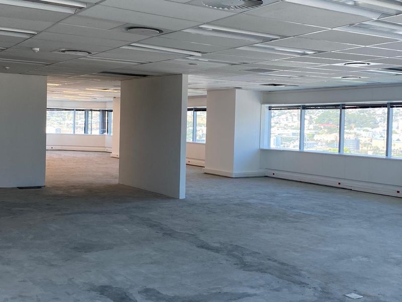 An expansive, open-plan office space featuring large windows with city views, suspended ceilings, and unfinished concrete flooring, ready for custom fit-out.