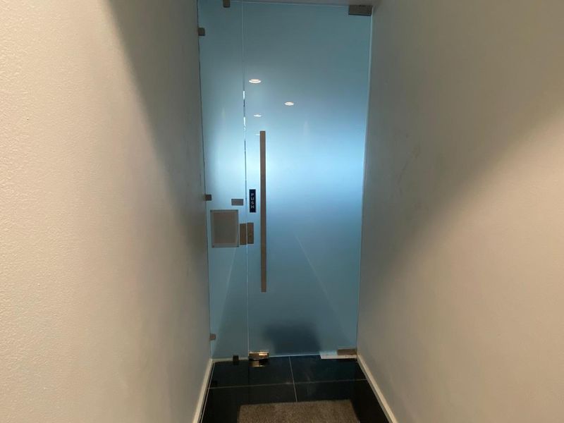 A modern office entrance featuring a sleek frosted glass door with a stainless steel handle and recessed ceiling lighting.