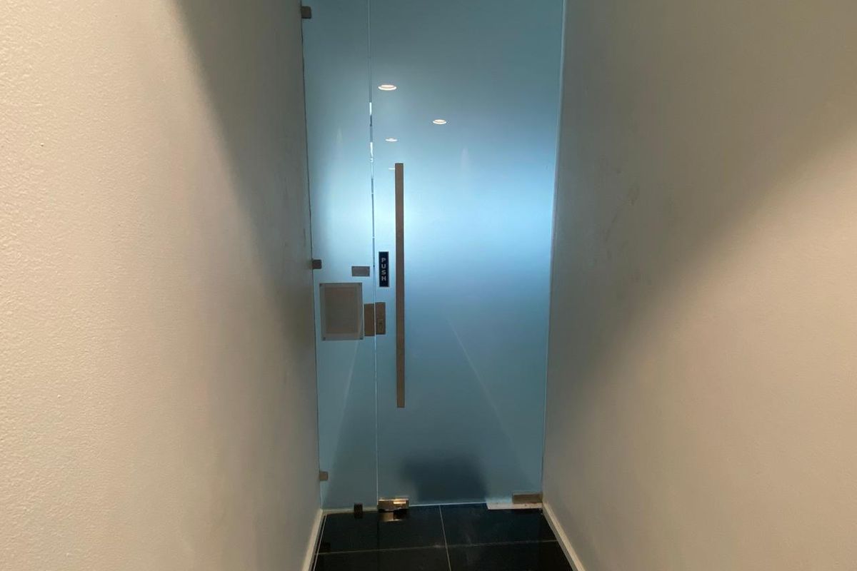 A modern office entrance featuring a sleek frosted glass door with a stainless steel handle and recessed ceiling lighting.