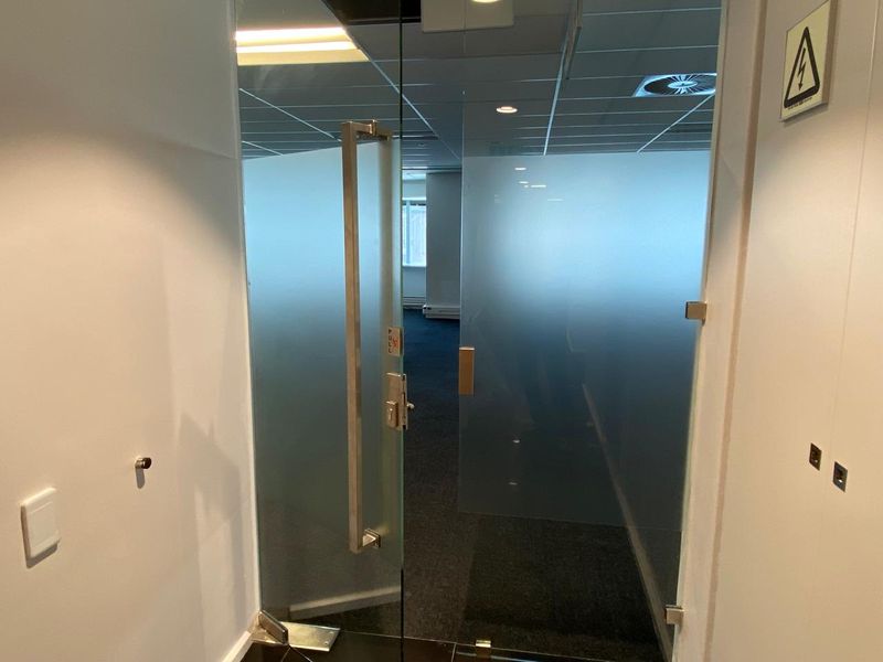 A professional office entrance featuring modern frosted glass double doors, carpeted flooring, and a suspended ceiling with recessed lighting.