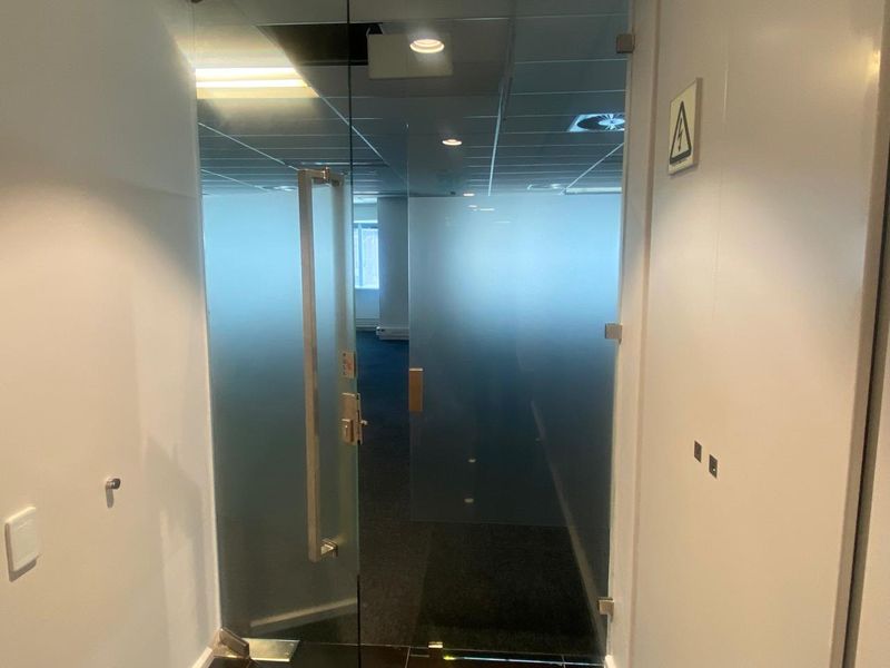A professional office entrance featuring a modern frosted glass door, suspended ceiling with recessed lighting, and clean carpeted flooring.
