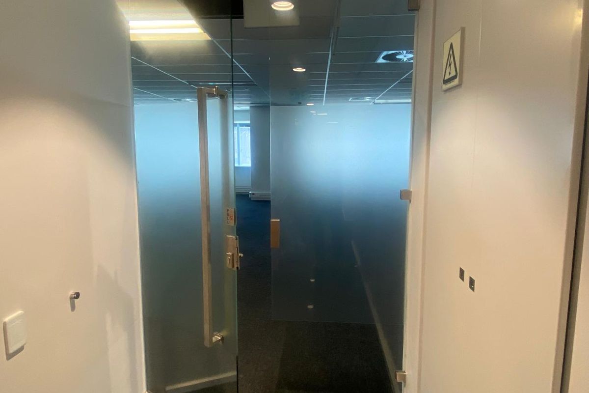 A professional office entrance featuring a modern frosted glass door, suspended ceiling with recessed lighting, and clean carpeted flooring.