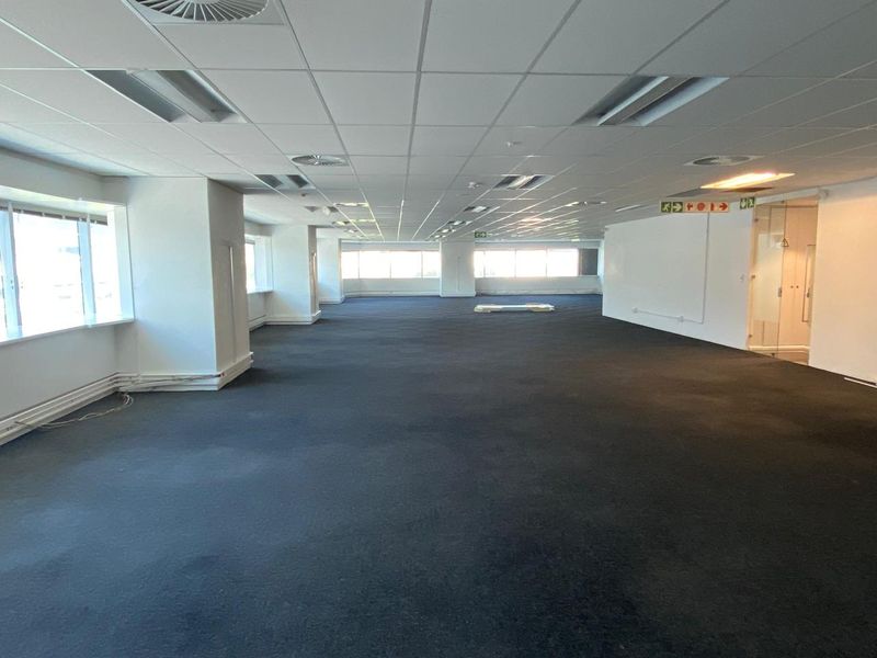 A spacious, open-plan office area featuring a suspended ceiling, recessed lighting, and large windows providing ample natural light.