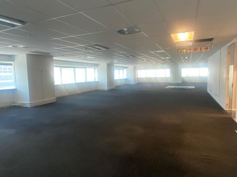 A spacious, open-plan office area featuring a suspended ceiling, recessed lighting, and large windows providing ample natural light.