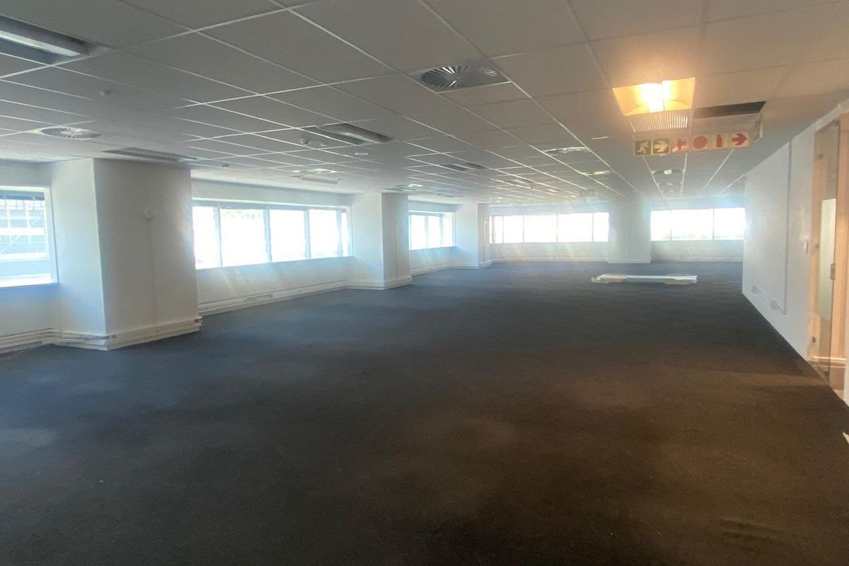 A spacious, open-plan office area featuring a suspended ceiling, recessed lighting, and large windows providing ample natural light.