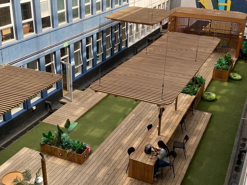 An elevated outdoor courtyard featuring timber decking, integrated wooden planters, artificial turf, and overhead timber pergolas providing shaded seating areas.
