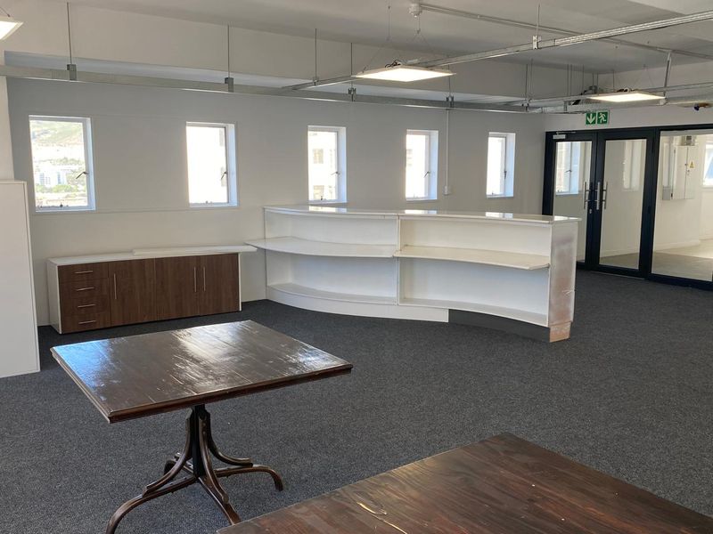Spacious office area featuring a built-in reception desk, integrated cabinetry, exposed industrial-style ceiling lighting, and glass-paneled double doors.