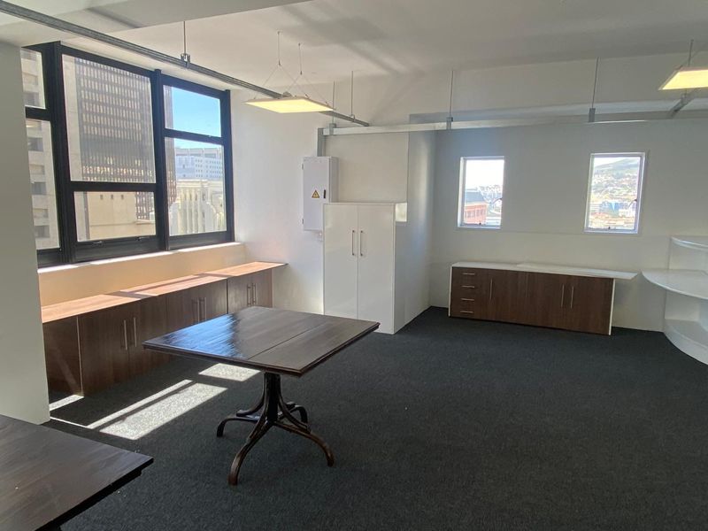 A bright office space featuring built-in cabinetry, dark carpeting, and large windows providing natural light and city views.