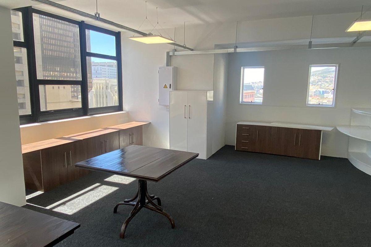 A bright office space featuring built-in cabinetry, dark carpeting, and large windows providing natural light and city views.