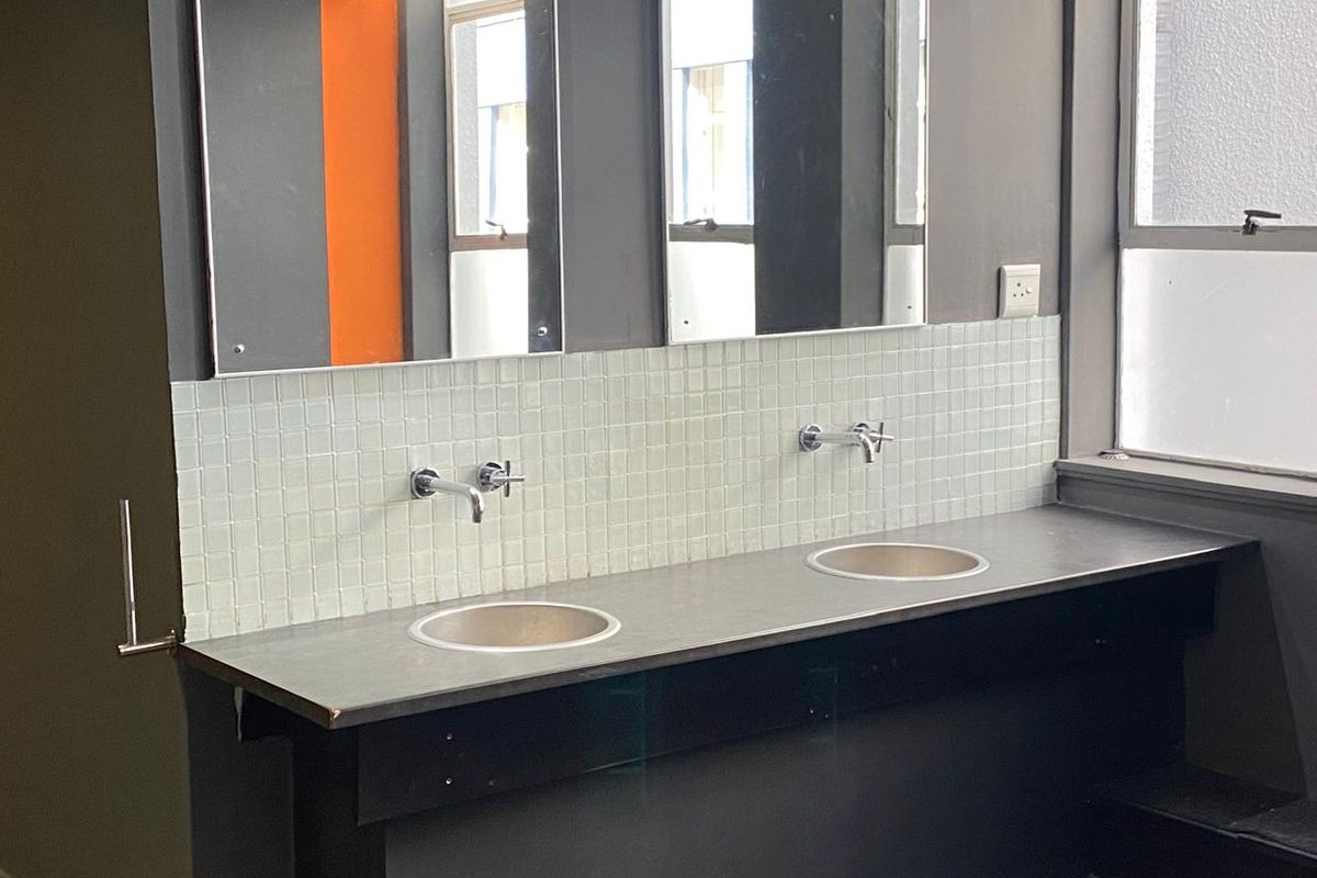 Commercial bathroom featuring a double vanity with wall-mounted faucets, mosaic tile backsplash, and integrated mirrors.