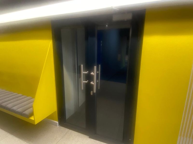 Modern commercial entrance featuring a double glass door with stainless steel handles and a vibrant yellow built-in bench seating area.