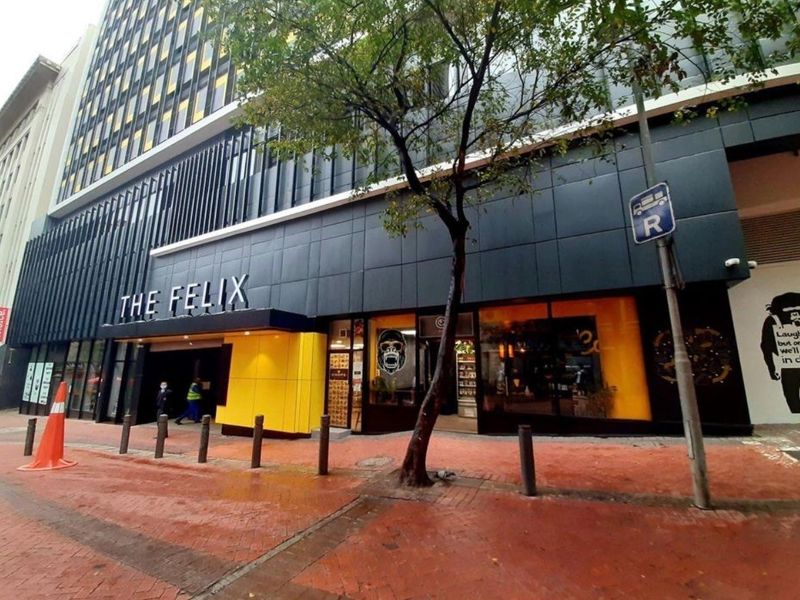 Modern commercial building facade featuring dark metal cladding, yellow accent panels, and large glass storefront windows at street level.