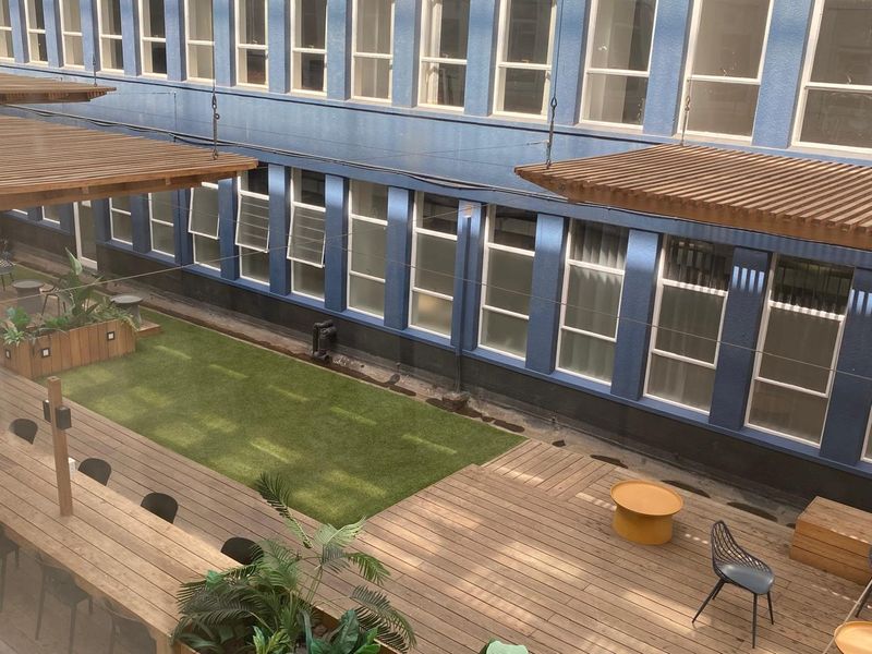 An elevated view of a commercial outdoor courtyard featuring timber decking, artificial grass, and a wooden pergola structure against a blue building facade.