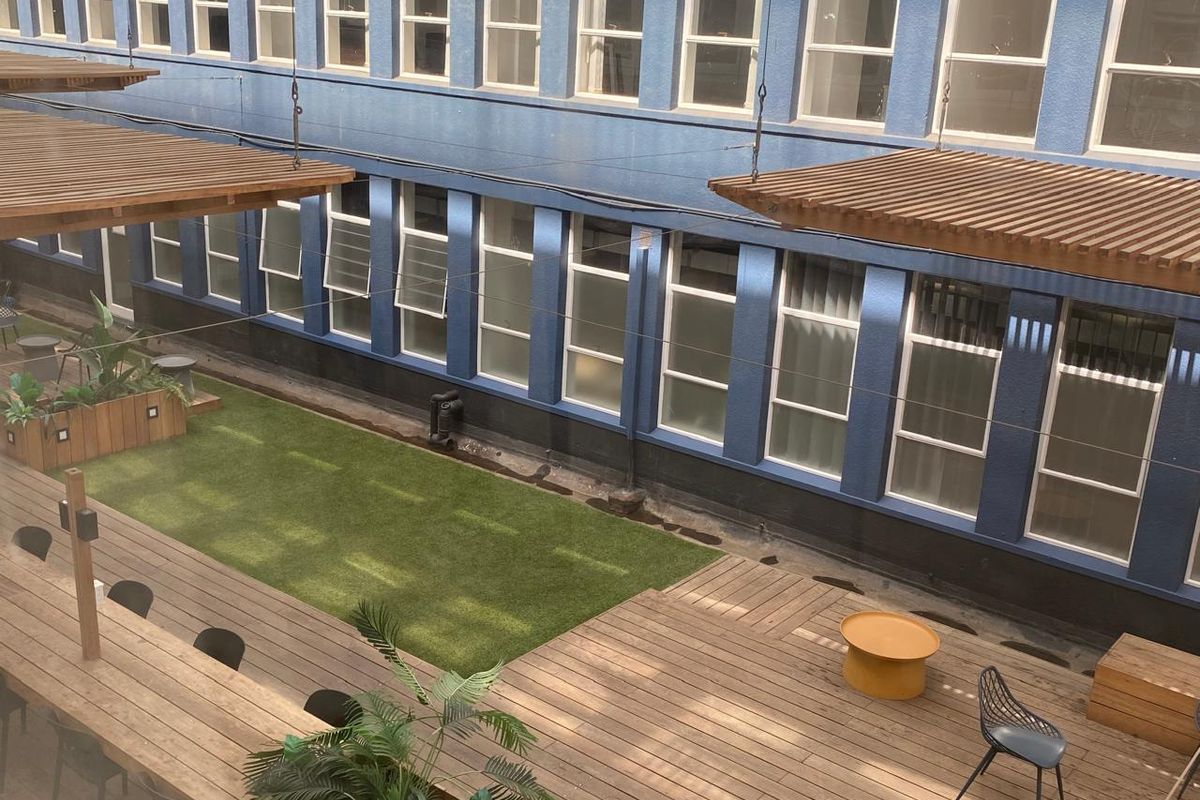 An elevated view of a commercial outdoor courtyard featuring timber decking, artificial grass, and a wooden pergola structure against a blue building facade.