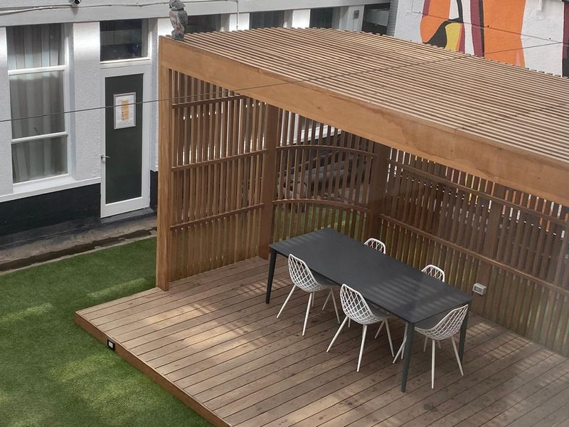 A well-maintained outdoor patio area featuring timber decking, a slatted timber pergola, and artificial turf, providing a modern and functional outdoor entertainment space.