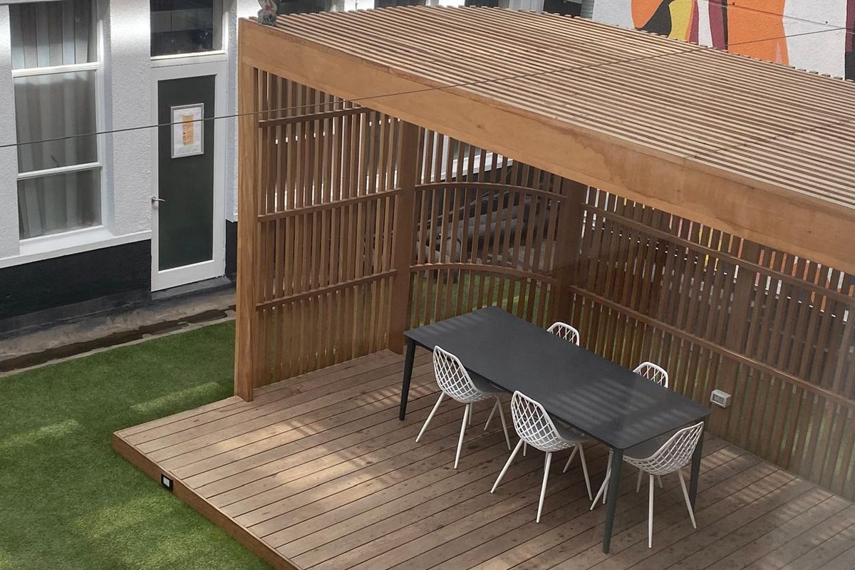 A well-maintained outdoor patio area featuring timber decking, a slatted timber pergola, and artificial turf, providing a modern and functional outdoor entertainment space.