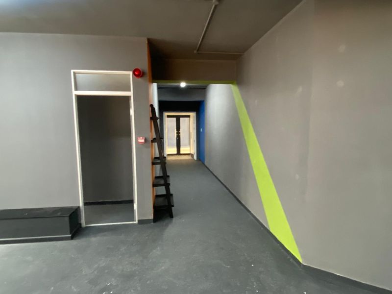 A commercial hallway featuring grey painted walls with lime green accents, fire safety equipment, and double glass doors at the end of the corridor.