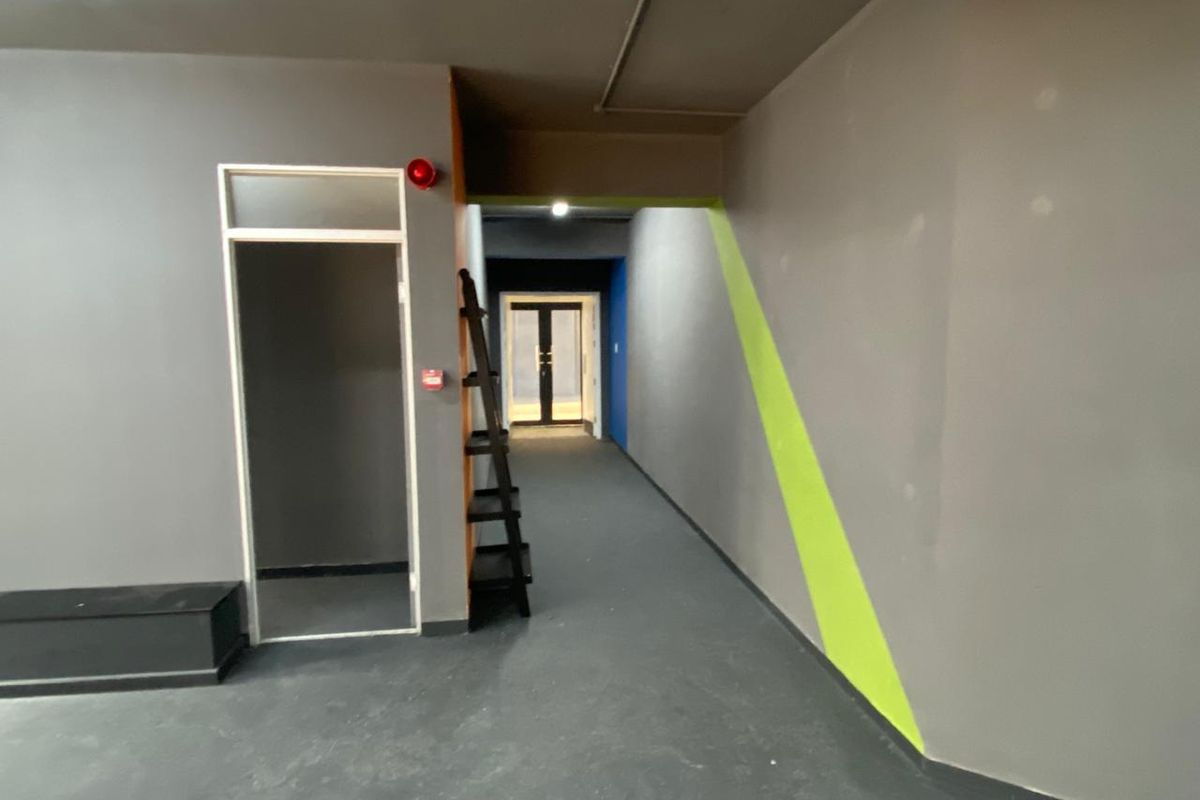 A commercial hallway featuring grey painted walls with lime green accents, fire safety equipment, and double glass doors at the end of the corridor.
