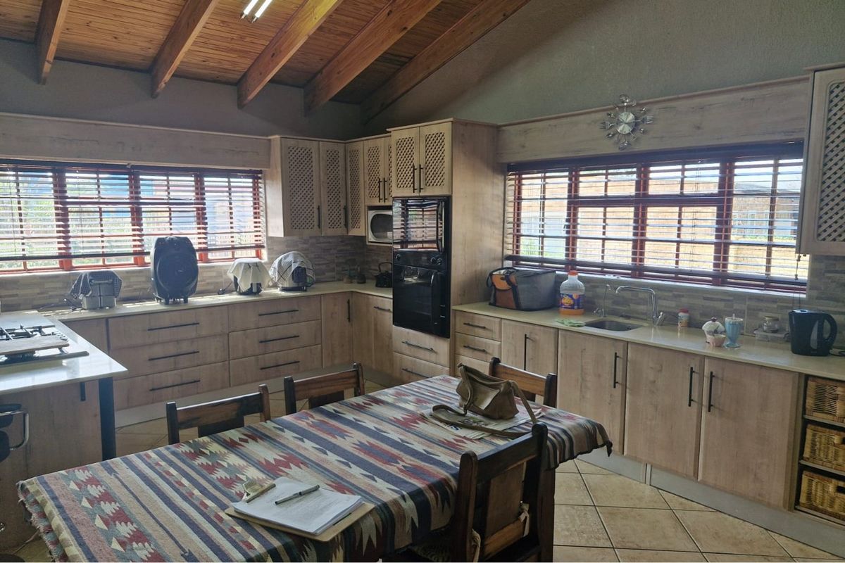 Spacious kitchen featuring light wood cabinetry, integrated appliances, tiled backsplash, and exposed timber ceiling beams, offering a functional and well-lit workspace.