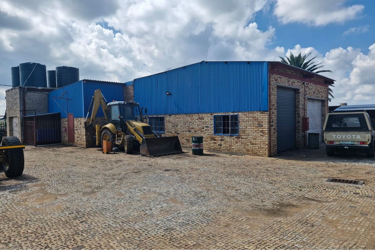 Commercial property exterior featuring face brick walls, blue corrugated metal cladding, roller shutter doors, and a paved yard area with water storage tanks.