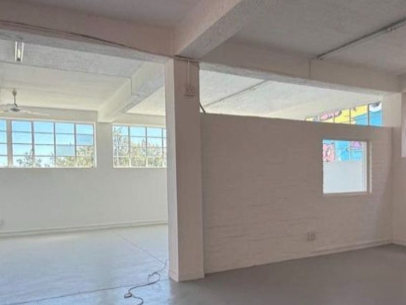 Spacious open-plan industrial unit featuring high ceilings with exposed beams, large steel-framed windows, and durable concrete flooring, offering a versatile workspace.