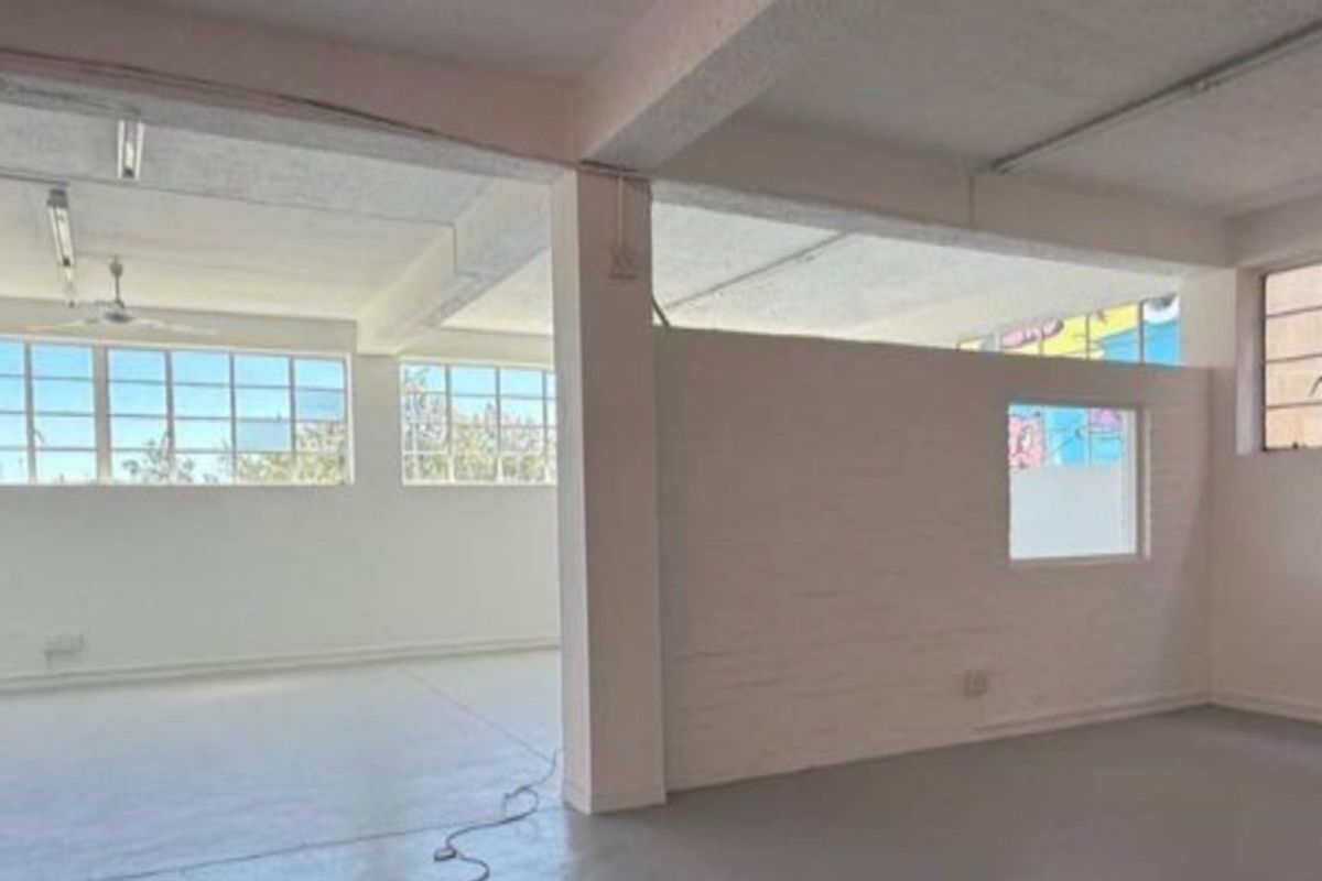 Spacious open-plan industrial unit featuring high ceilings with exposed beams, large steel-framed windows, and durable concrete flooring, offering a versatile workspace.