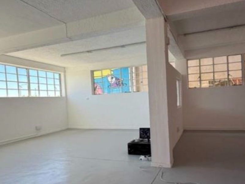 Spacious open-plan industrial unit featuring high ceilings with exposed beams, large steel-framed windows, and durable painted concrete flooring.