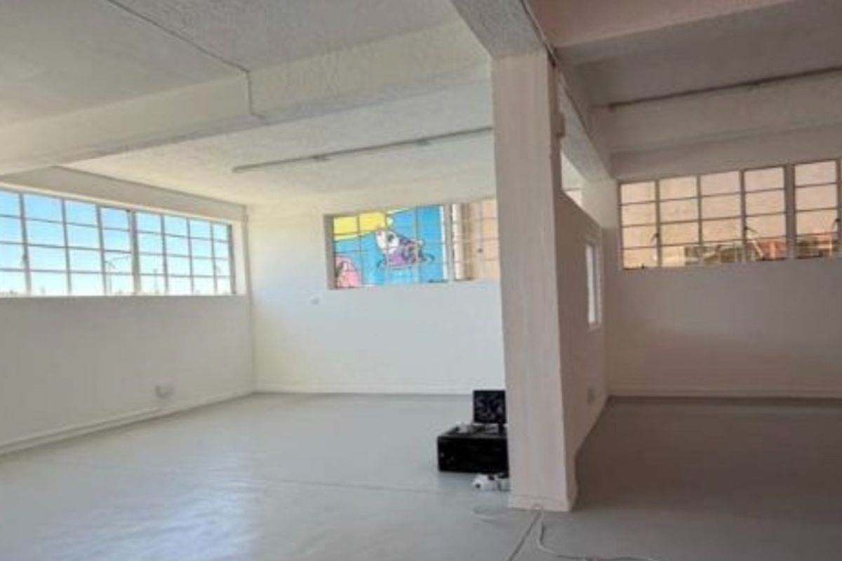 Spacious open-plan industrial unit featuring high ceilings with exposed beams, large steel-framed windows, and durable painted concrete flooring.