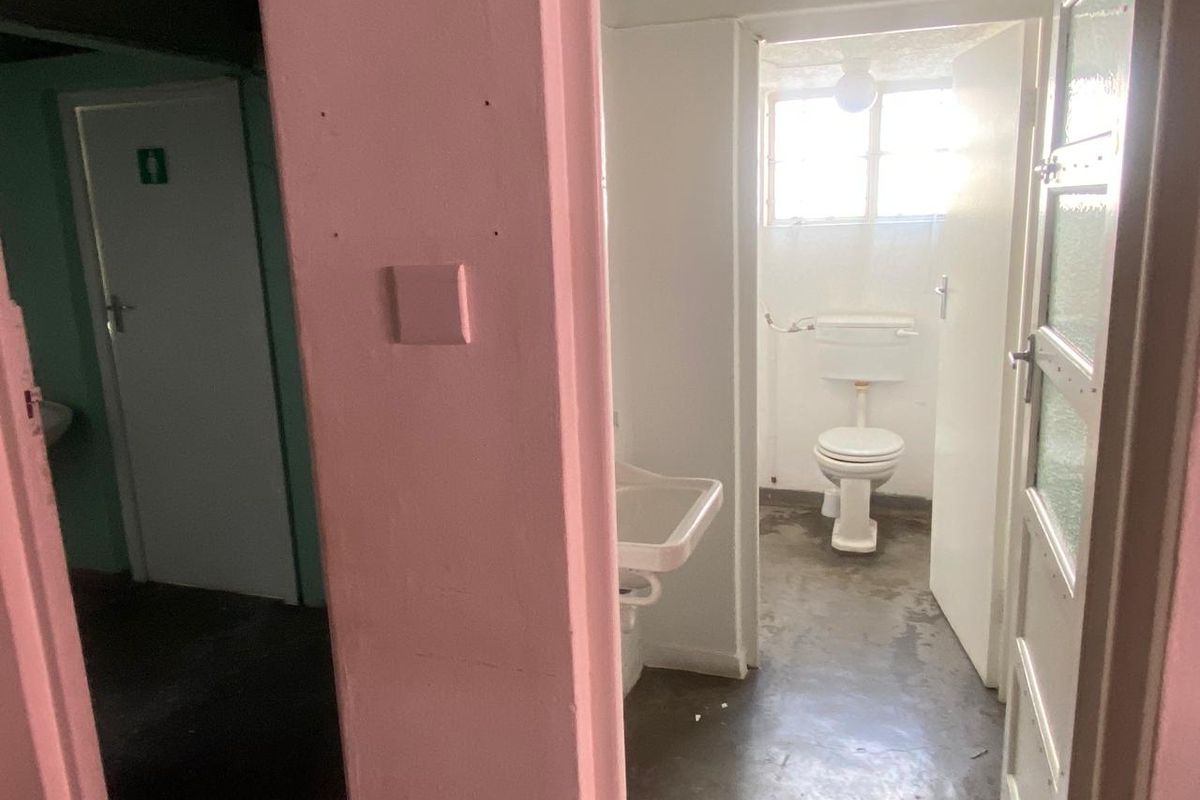 A functional industrial restroom facility featuring a basic toilet and wall-mounted basin with exposed plumbing and concrete flooring.