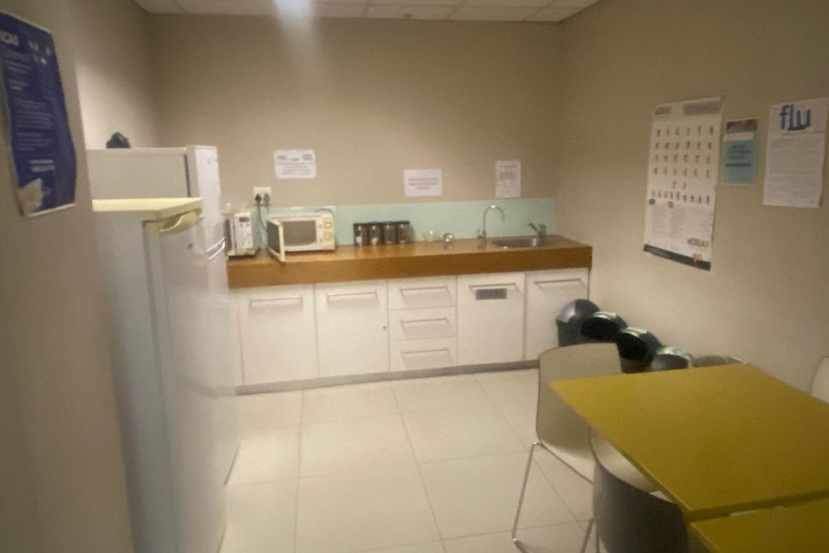 A functional office kitchenette featuring white cabinetry, a wooden countertop, a stainless steel sink, and a tiled floor.