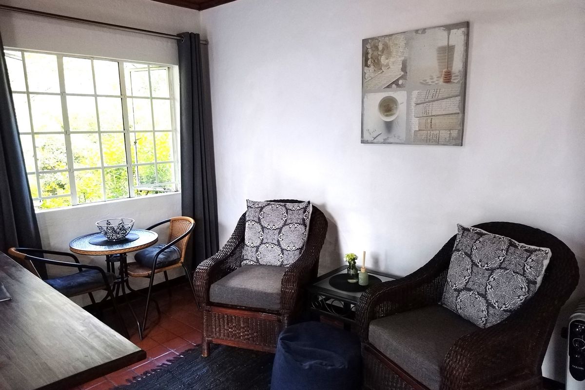A cozy living area featuring terracotta tiled flooring and a large window that provides natural light and garden views.