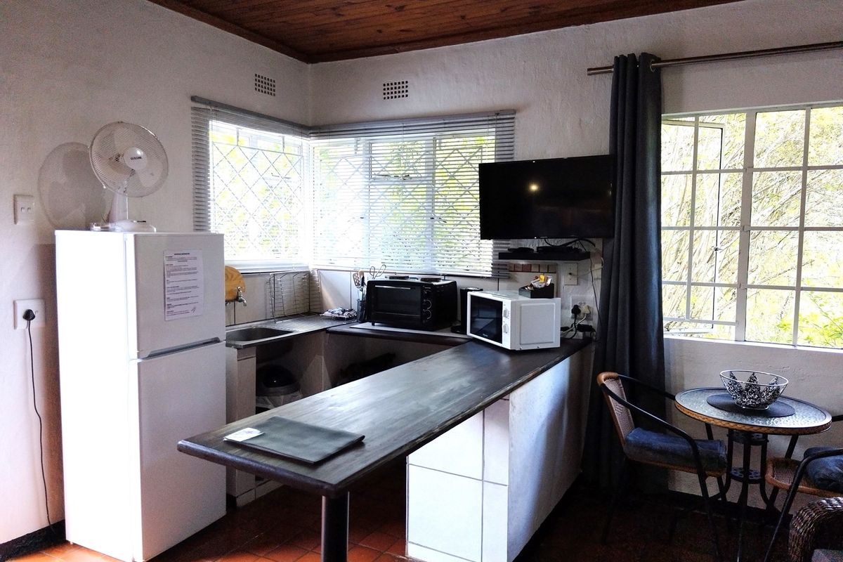 Compact kitchen area featuring a breakfast bar, built-in sink, and tiled flooring, set within an open-plan living space with natural light.