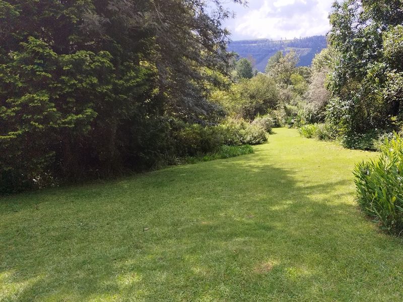 A lush, well-maintained garden area featuring expansive green lawns, mature trees, and scenic mountain views in the background.