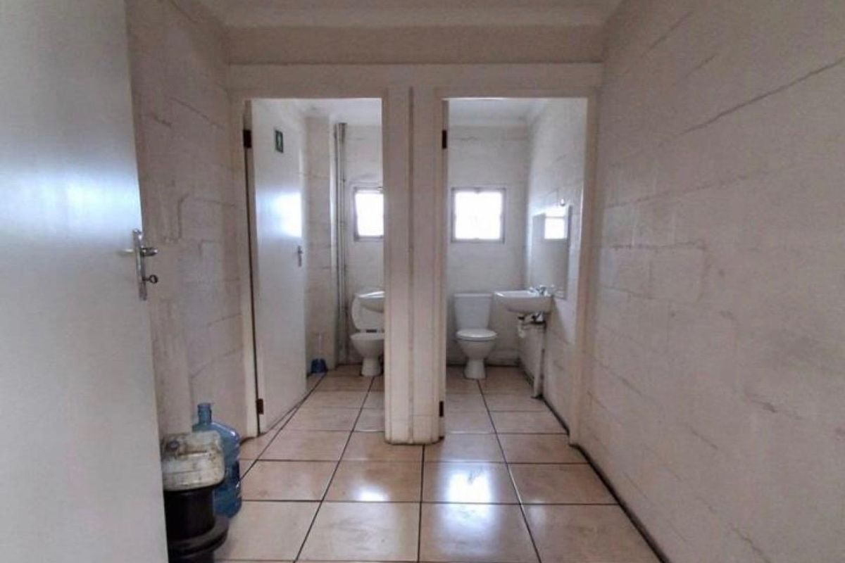Functional industrial-style bathroom facility featuring dual toilet cubicles with tiled flooring and exposed blockwork walls.