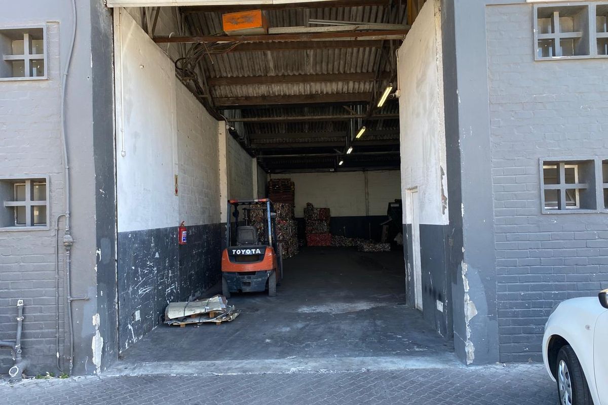 Industrial warehouse unit featuring a large roller shutter door, exposed steel roof structure, and concrete flooring, suitable for storage or light industrial operations.