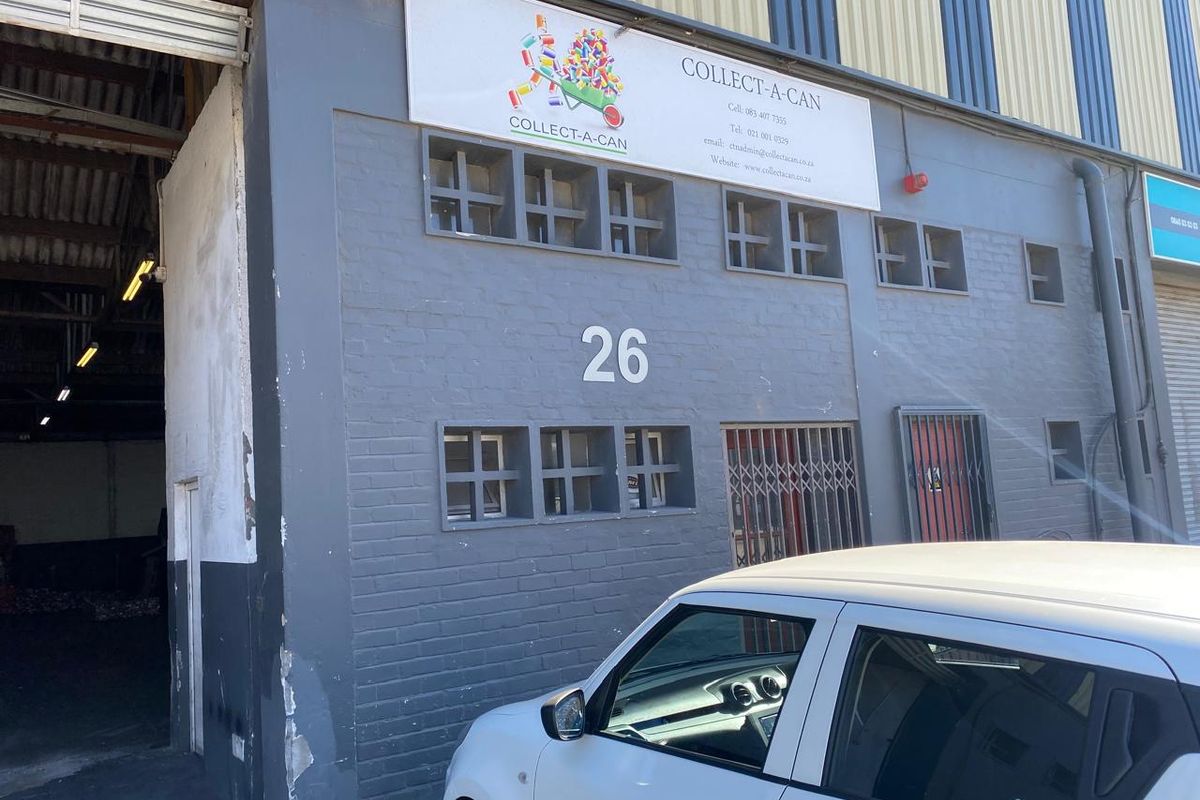 Front elevation of an industrial unit featuring a large roller shutter door, security gate, and prominent business signage on a painted brick facade.