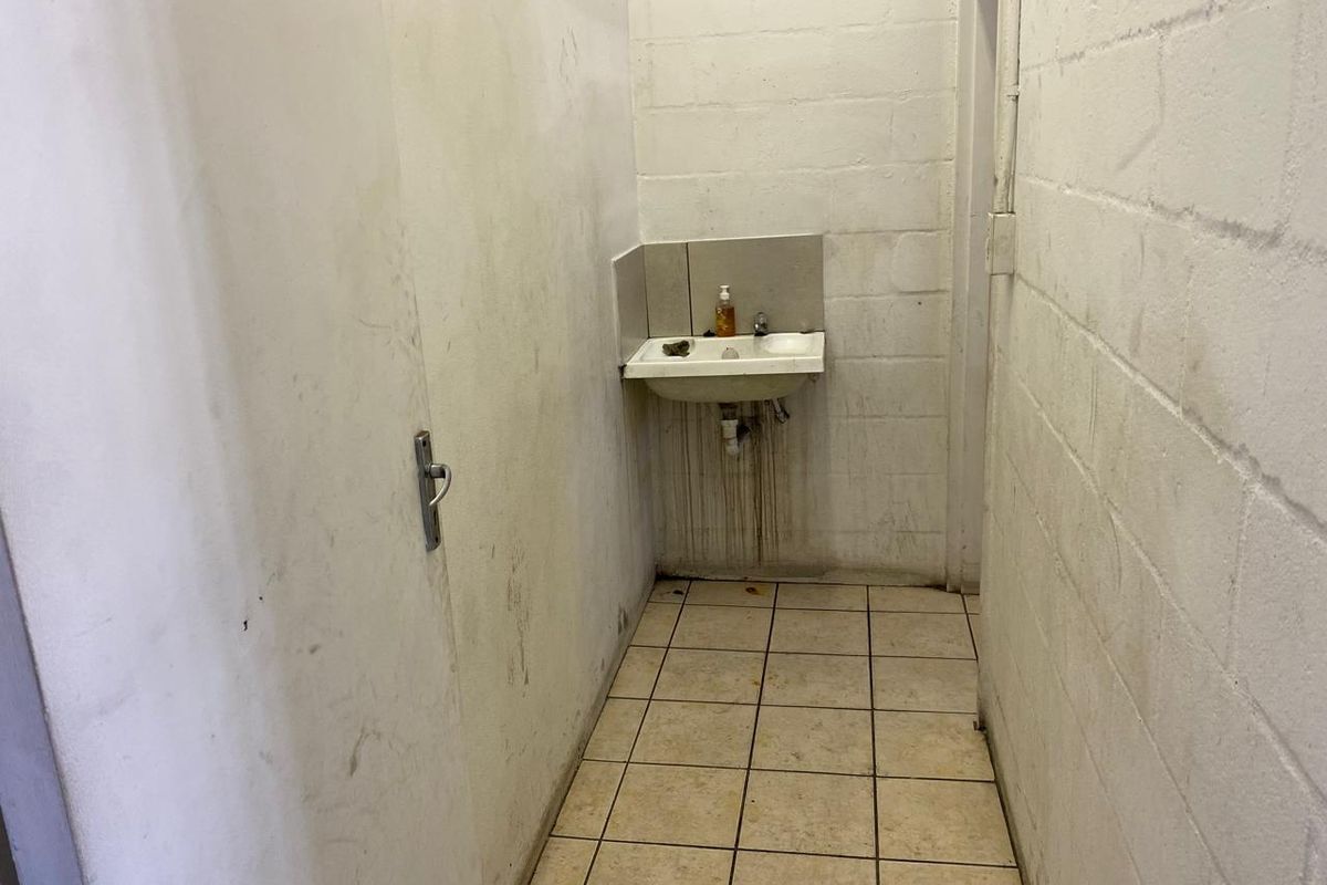 A basic industrial bathroom area featuring a wall-mounted basin, tiled flooring, and exposed cinder block walls in need of maintenance and refurbishment.