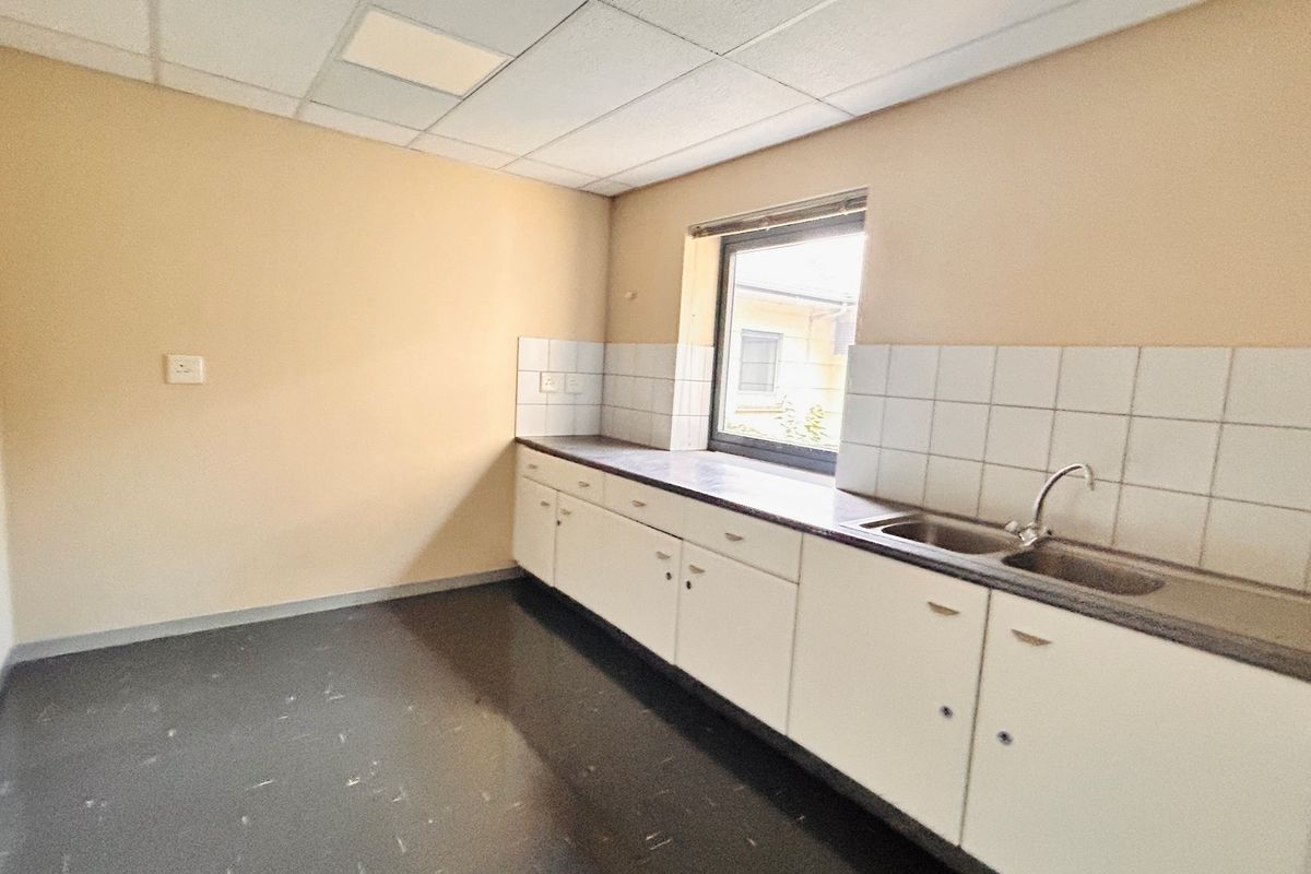 A functional office kitchenette featuring built-in cabinetry, a stainless steel sink, tiled splashback, and a suspended ceiling.