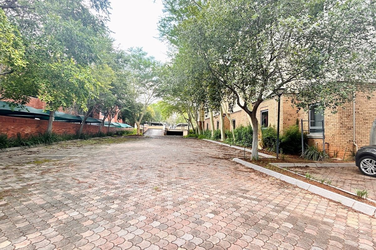 Exterior view of an office property featuring a paved driveway, brick facade, and established trees with shade cloth parking structures.