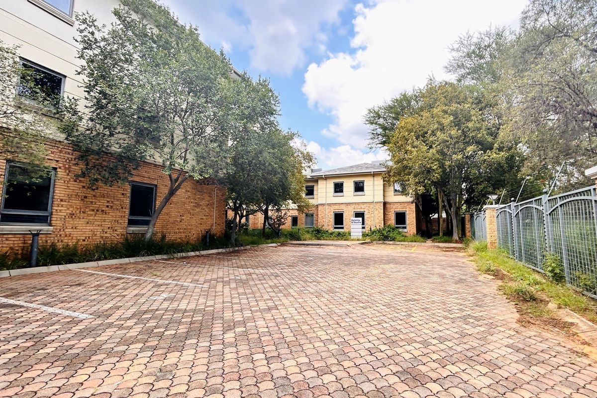 Exterior view of an office building featuring a paved parking area, brick facade, and perimeter security fencing.
