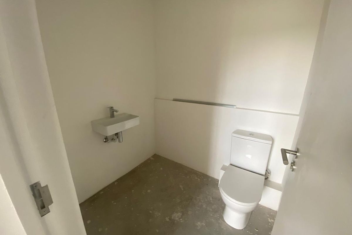 A compact, unfinished restroom featuring a wall-mounted basin and a standard toilet, currently in a basic shell condition.