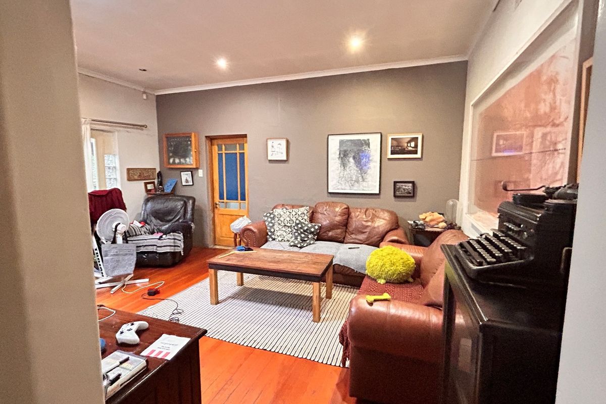 A comfortable living room featuring polished timber flooring, recessed downlighting, and a classic wooden door, providing a warm and inviting office lounge space.