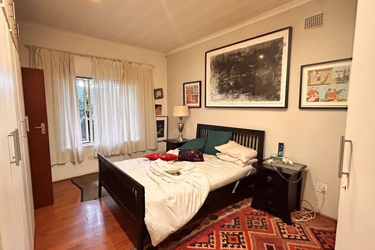 A bedroom featuring wooden flooring, built-in cupboards, and a window with curtains, providing a functional and comfortable living space.