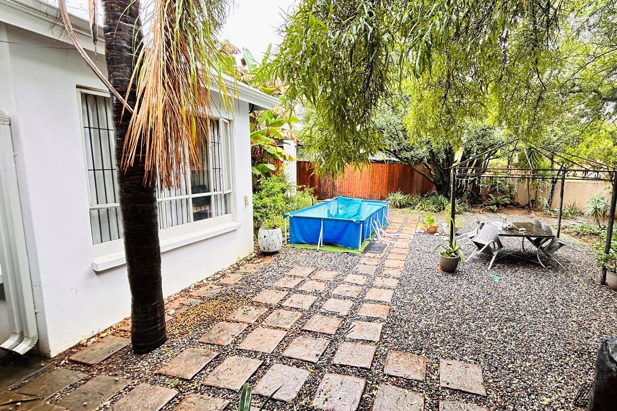 A rear garden area featuring a gravel pathway, paved stepping stones, mature trees, and a portable pool set within a fenced backyard.
