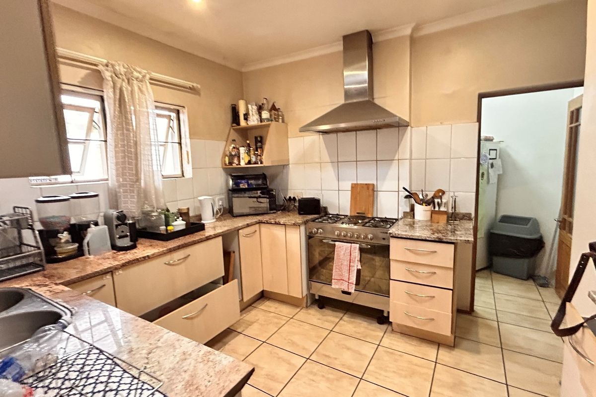 Functional kitchen featuring granite countertops, a stainless steel extractor fan, gas stove, and tiled flooring with ample built-in cabinetry.