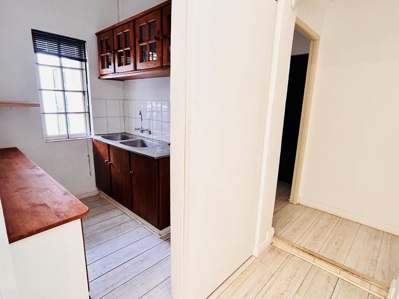 A functional scullery area featuring built-in wooden cabinetry, a double stainless steel sink, and light-toned laminate flooring.