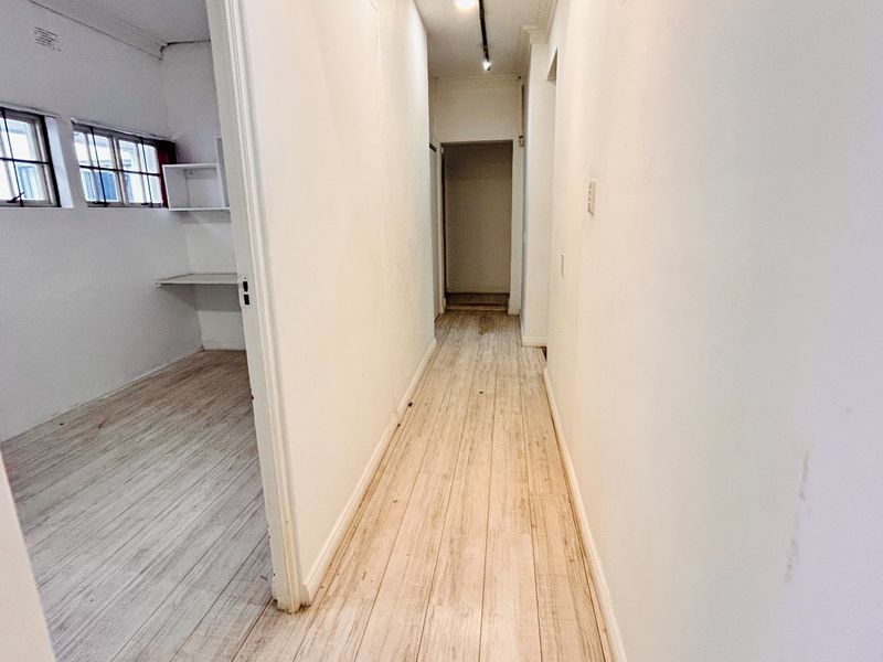 A vacant hallway leading to an office space with laminate flooring, built-in desk, and casement windows.