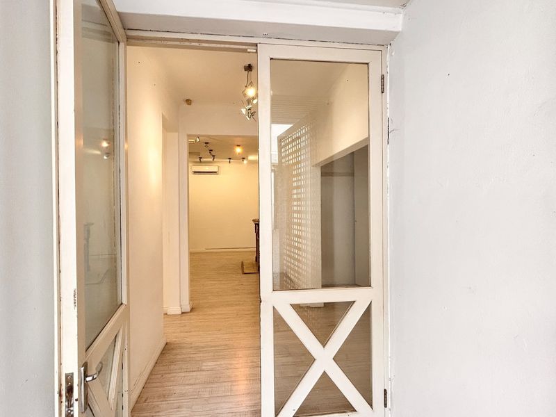 An inviting office entrance featuring glass-paneled double doors, light-toned laminate flooring, and a bright, open-plan interior space with modern recessed lighting.